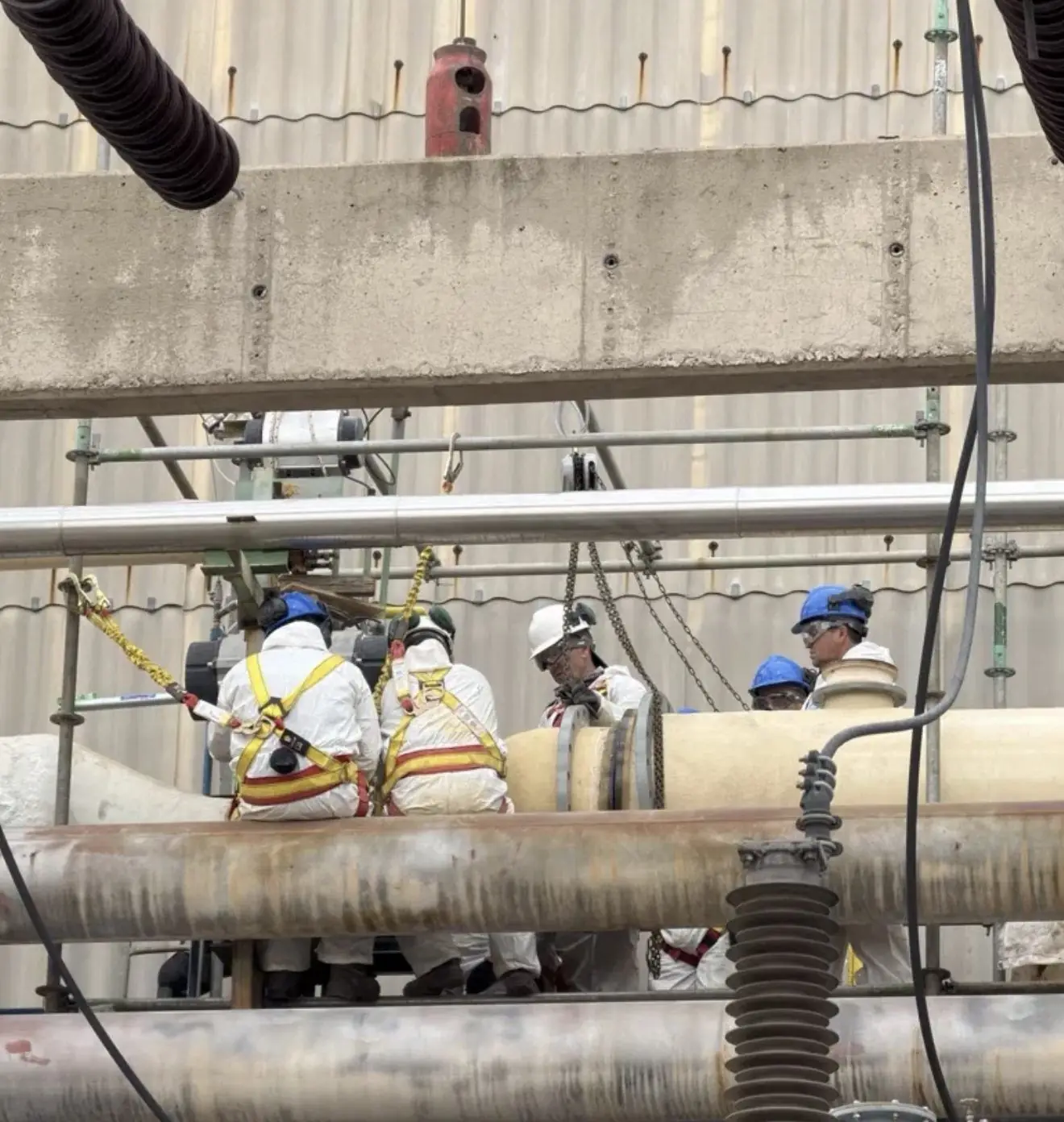 Operarios con arnés y casco maniobran una cañería de PRFV con aparejos de cadena
